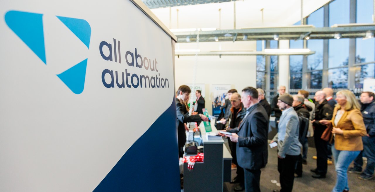 Im Vordergrund Logo der all about automation Messe, im Hintergrund viele Menschen
