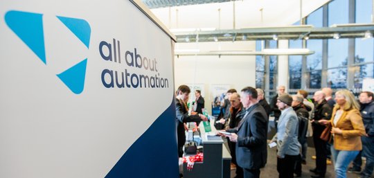 Im Vordergrund Logo der all about automation Messe, im Hintergrund viele Menschen